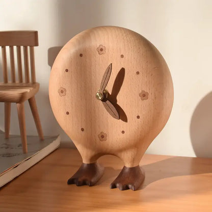 The Senser Woodcraft - Big Foot Clock - LL56, with carved flower numbers, leaf-shaped hands, and dark wooden feet, sits beside a miniature chair and a closed book, bringing unique charm to your handcrafted home decor.