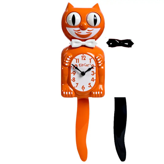 The California Clocks Kit-Cat Klock - Orange Harvest (BC-60) is a limited edition clock featuring an orange cat-shaped design with a crisp white bowtie, moving eyes, and a wagging tail. An additional black tail is shown to the right of the clock.