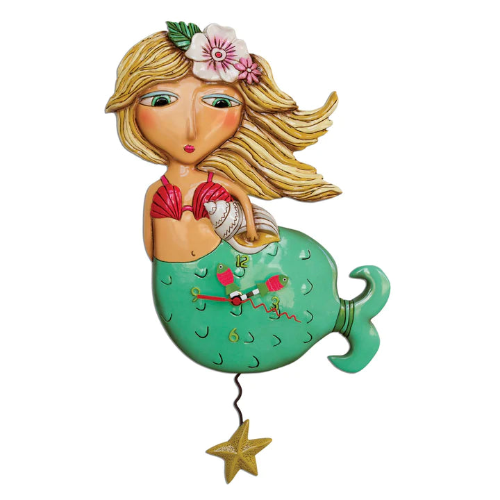 The Enesco Allen Designs Clock - Shelley Mermaid (P1610) features a long-blonde-haired mermaid with a pink flower, green tail, and seashell. A yellow starfish-mermaid pendulum swings below, and the clock hands are set on her tail.