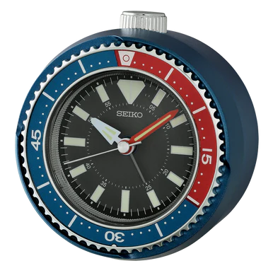 The Seiko - Mai Modern Alarm Clock (QHE207L) by Seiko is a round alarm clock designed with a blue and red bezel, black dial, bold hour markers, and white hands reminiscent of a diver’s watch. It features reliable quartz movement and a quiet sweep second hand for precise, silent timekeeping without the disruptive ticking.