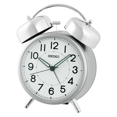 The Seiko Clocks - Bedside Alarm - QHK063SLH is a silver bedside clock with two bells on top, black numbers, and three hands set at 10:09:37. It features a quiet sweep second hand and stands on two small legs.