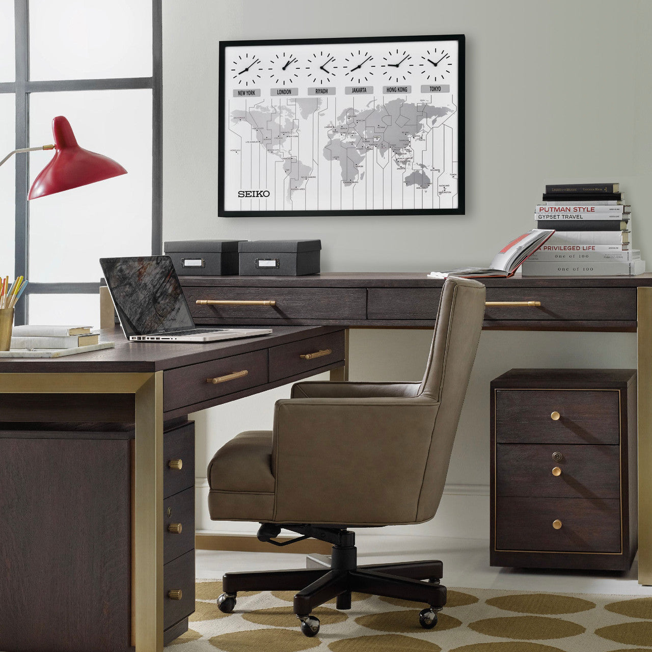 A modern office features a dark wood desk, brown swivel chair, red desk lamp, and neatly arranged books and boxes. On the wall is a Seiko World View Wall Clock (QXA538KLH) by Seiko showing multiple time zones. Storage drawers are nearby.