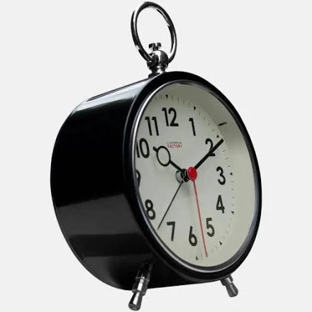 The Cloudnola Clock - Factory Black Alarm Clock (SKU0116) by Cloudnola features a vintage style with a white face, black numbers, and silver legs. Pictured at an angle on a white background, the clock displays the time as approximately 2:10.