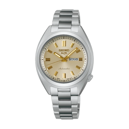 The Seiko 5 SRE023 is a silver automatic watch from Seiko, featuring a stainless steel band, gold hour markers and hands, a beige dial, and a day-date window at 3 o’clock showing MON 6.