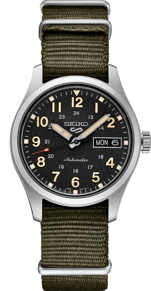 The Seiko 5 Sports SRPJ85 is a Seiko field watch with a black dial, white/beige numerals, silver hands, day-date display, and an olive green NATO strap. Automatic appears above 6 o’clock.