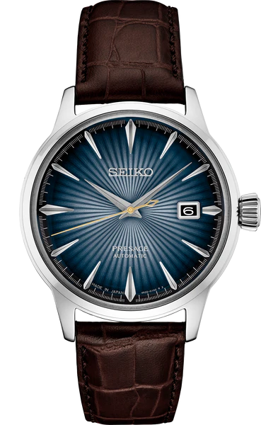 The Seiko Presage Cocktail Time SRPK15 is a Japanese mechanical watch featuring a blue sunburst dial, silver hour markers and hands, date window at 3 o’clock, and brown leather strap. The face is labeled "Presage Automatic.