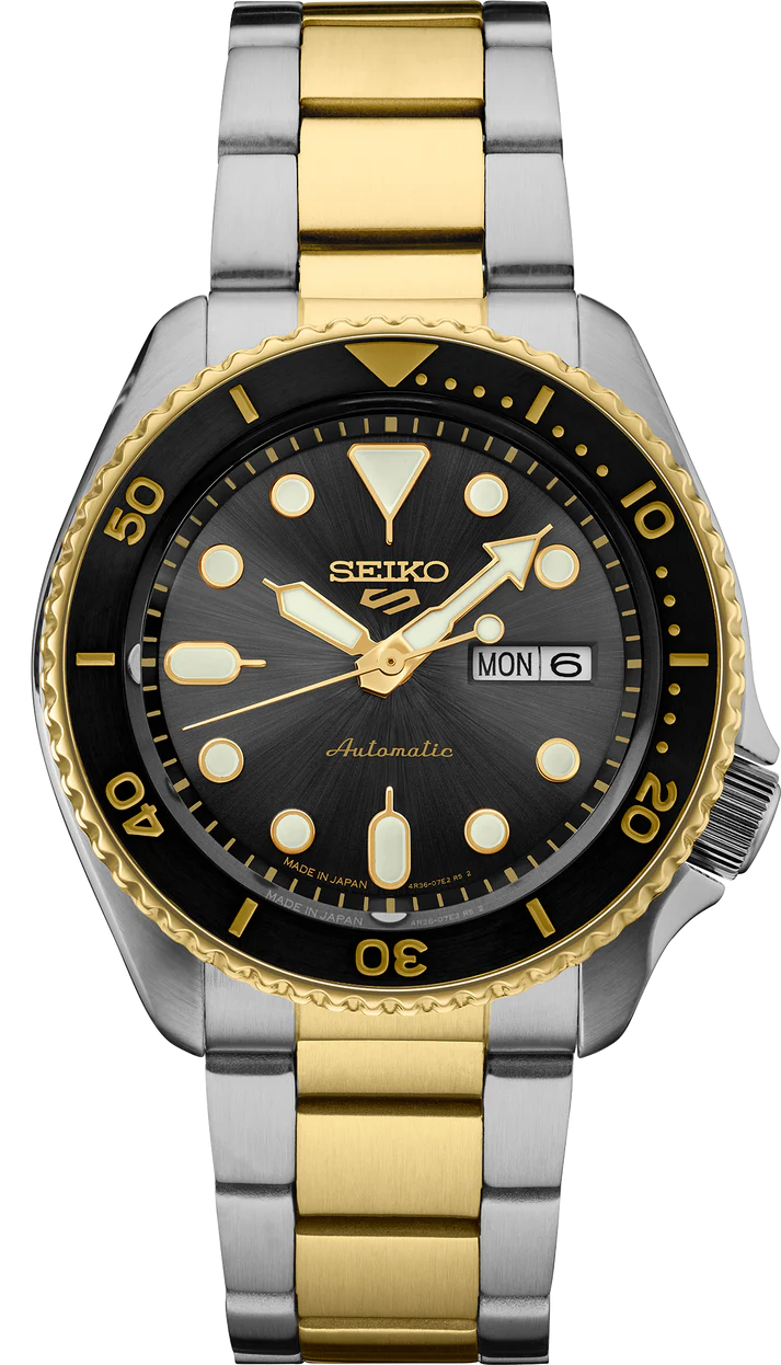 The Seiko 5 - SRPK22 by Seiko features a silver and gold stainless steel band, black and gold bezel, black dial with gold accents, and day/date display at 3 o’clock.