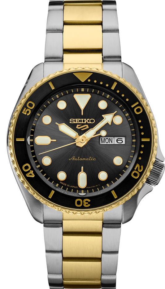 The Seiko 5 - SRPK22 by Seiko features a silver and gold stainless steel band, black and gold bezel, black dial with gold accents, and day/date display at 3 o’clock.