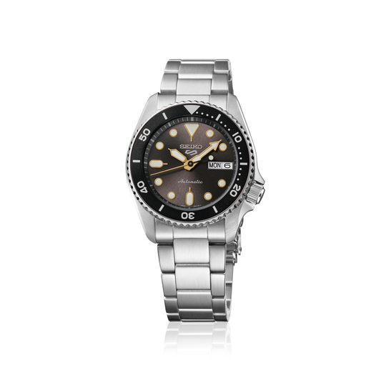 The Seiko Watch - Seiko 5 Sports - SRPL79 is a silver automatic timepiece with a black bezel and dial, luminous hour markers, stainless steel bracelet, and day-date display on the right.
