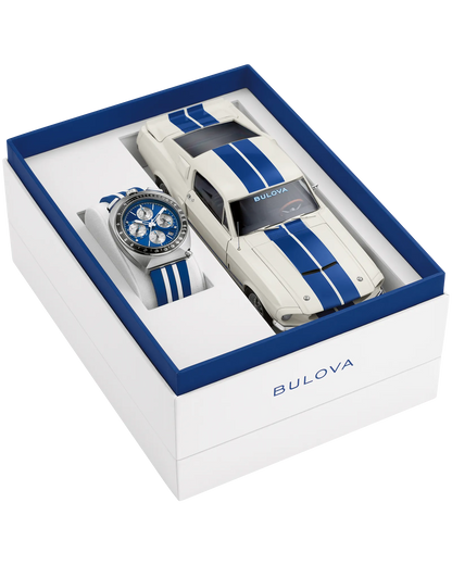 The Bulova Shelby Racing Chronograph (98B452) gift set includes a blue and white limited-edition watch and a matching white model car with blue stripes, both in an elegant box with blue accents and the Bulova logo.