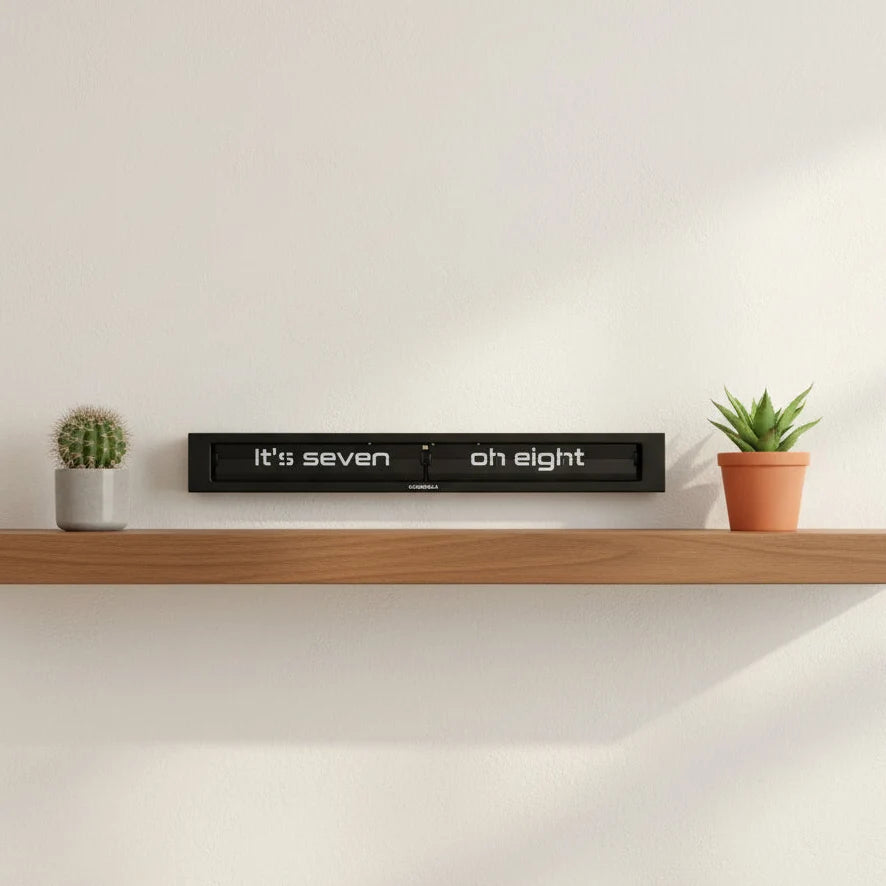 A wooden shelf displaying a small cactus, a potted succulent, and the Cloudnola Texttime Black Flip Clock (0072) by Cloudnola showing 7:08, set against a plain white wall.