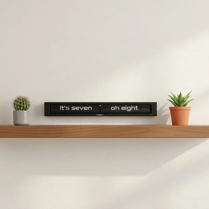 A wooden shelf displaying a small cactus, a potted succulent, and the Cloudnola Texttime Black Flip Clock (0072) by Cloudnola showing 7:08, set against a plain white wall.