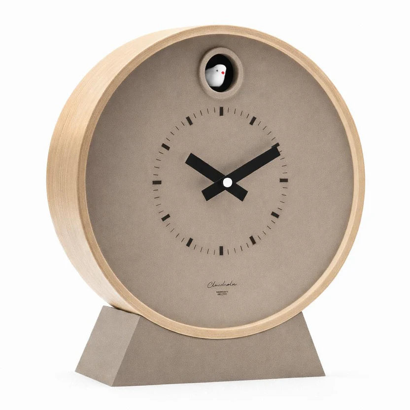 The Cloudnola Clock - Taupe Dot Cuckoo Clock (0286) by Cloudnola features a light wood frame, beige face, black minimalist hands and hour marks, a matching base, and a small white bird in a circular top window.