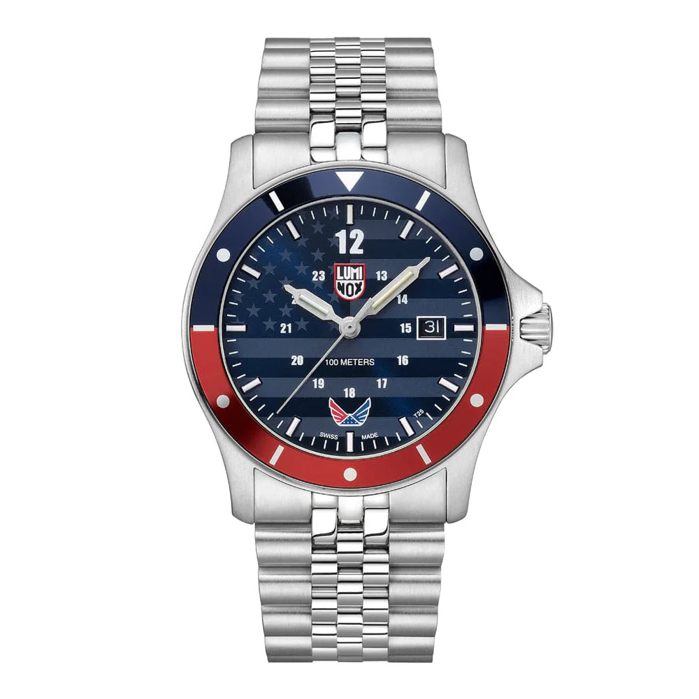 The Luminox Watch - Minuteman - XS.0914.VOL showcases a silver wristband, blue dial, white hour markers, red and blue bezel, and an American flag design—reflecting the VOLITION AMERICA spirit and featuring date display.