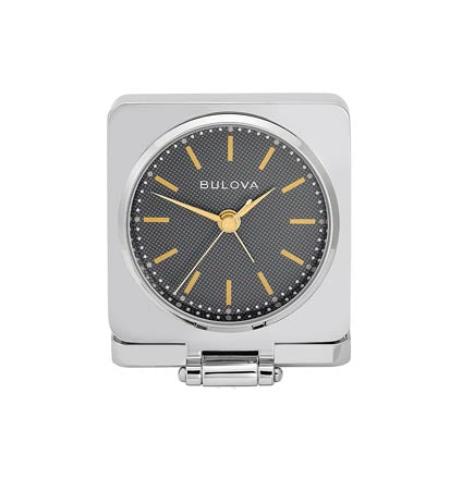 The Bulova Clock - Traveler (B1879) is a square silver travel alarm clock with a round black textured face, gold hour markers and hands, plus a hinged stand—an elegant, engravable gift ideal for any journey.