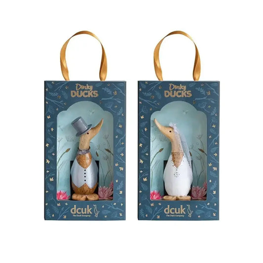 The Enesco DCUK Ducks Dinky Wedding Set (6018580) features two boxed bamboo ducks dressed as bride and groom, with a gray top hat and bow tie, white veil, blue box designs, and gold ribbon handles—ideal as wedding favors.